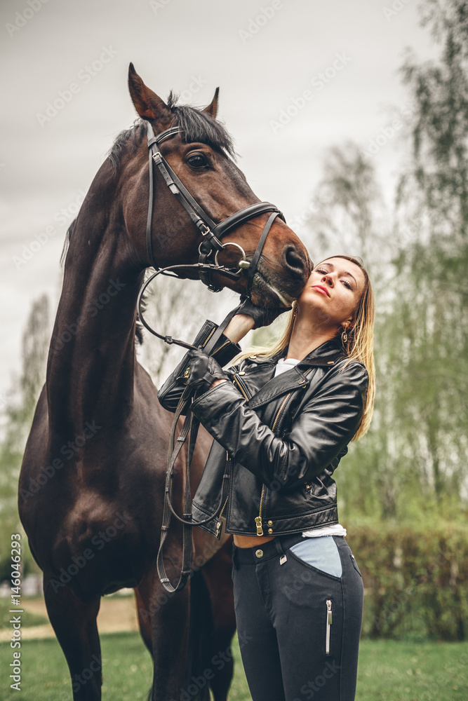 Obraz premium Beautiful girl communicates with the horse in the park. Preparing for the riding