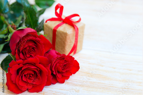 Bouquet of red roses flowers and gift box with ribbon and bow on wooden background. Concept for Happy mother´s day greeting card. Space for your text.