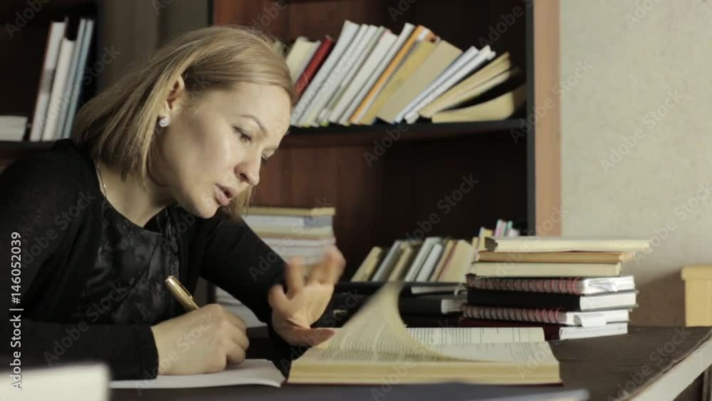 Focused female student working with books in a library in university college. tired student preparing for exams Focused female student working with books in a library in university college. tired student preparing for exams