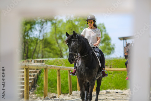 Lovely young brunette with sunglasses, riding a horse