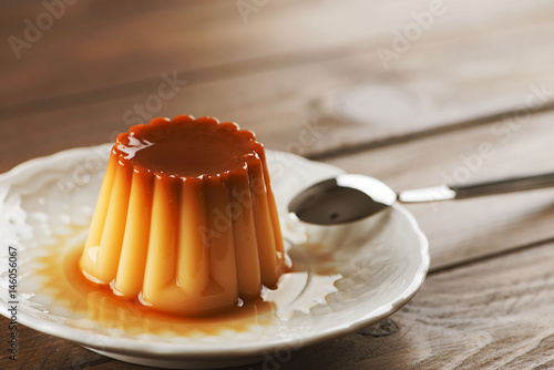 From above white plate with flan and spoon on the wooden background. Horizontal shoot. photo