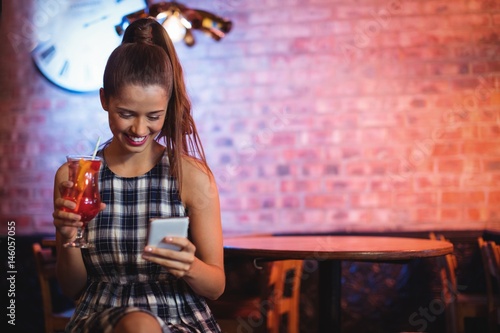 Young woman using mobile phone while having cocktail drink