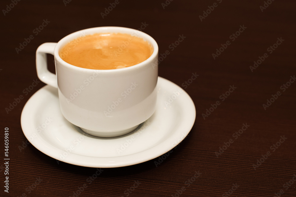 White cup with cappuccino on a saucer on a wooden table White cup with cappuccino on a saucer on a wooden table
