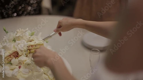 Bride cuts wedding cake with glaze roses and puts it on guest's plate