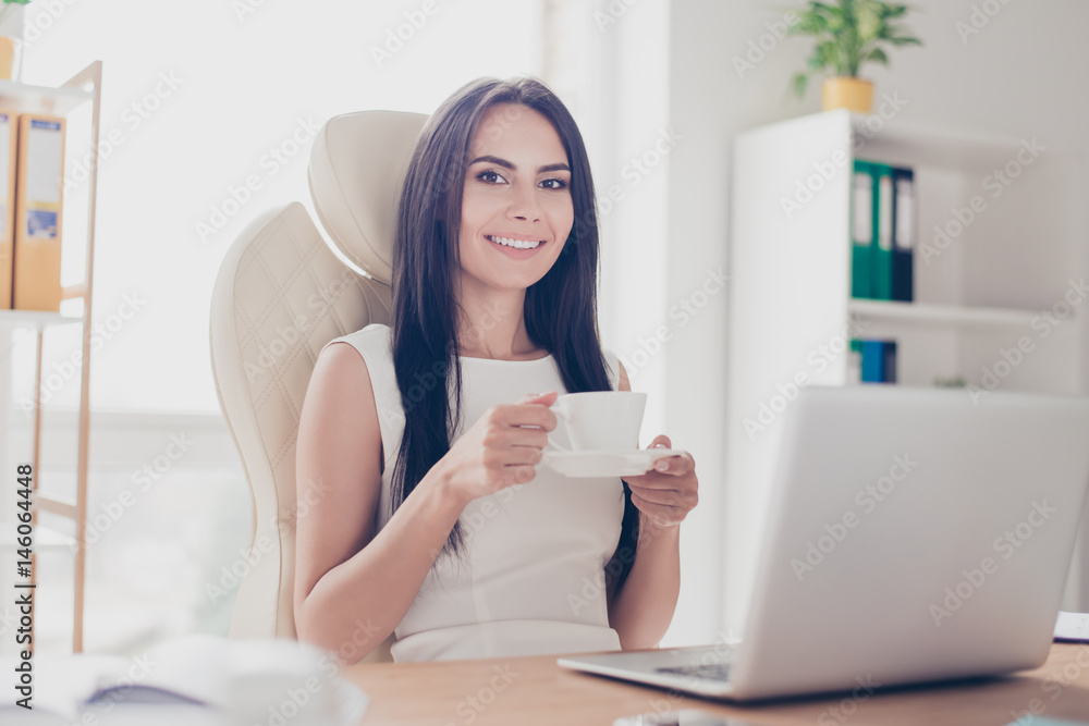 Young attractive business lady is having a cup of coffee at her workplace. She is happy and thinking of the vacation which is coming Young attractive business lady is having a cup of coffee at her workplace. She is happy and thinking of the vacation which is coming