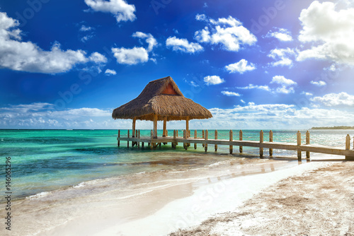 Tropical white sandy beach. Palm leaf roofed wooden pier with gazebo on the beach. Punta Cana, Dominican Republic