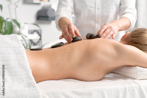 Woman getting hot stone massage in spa salon.