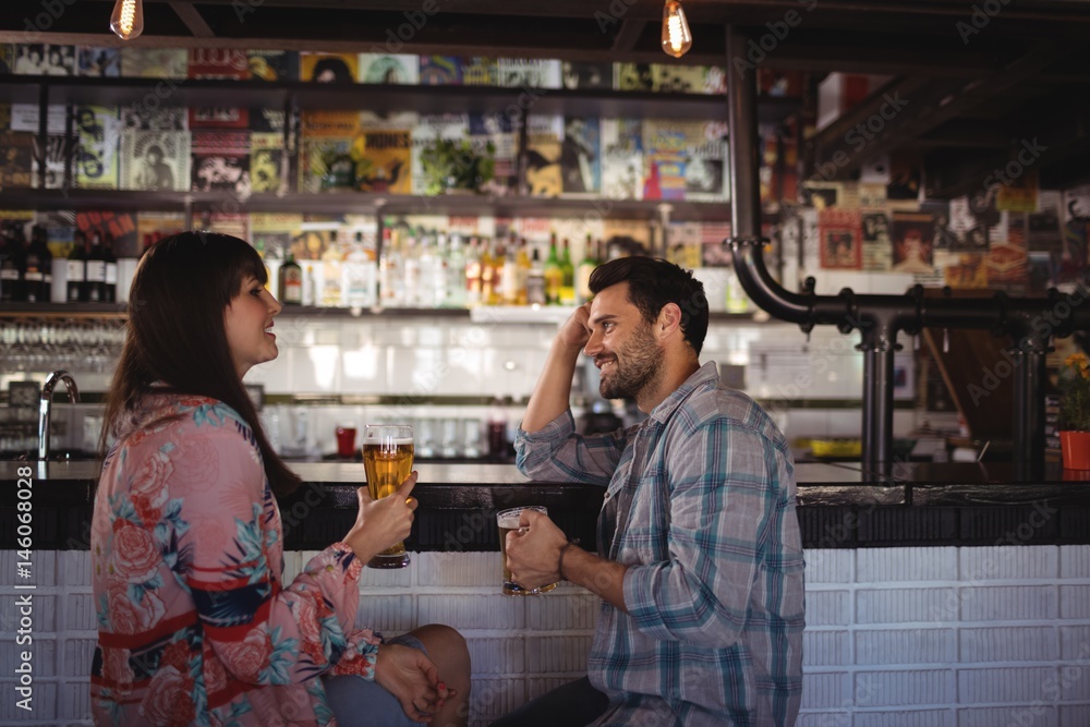 Happy couple interacting while having beer at counter