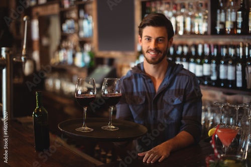 Portrait of bar tender holding a tray with glasses of red wine