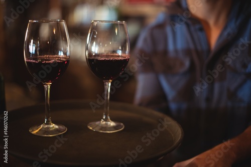 Bar tender holding a tray with glasses of red wine