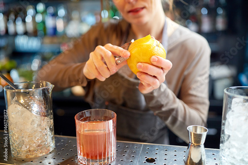 Fototapeta bartender peels orange peel for cocktail at bar