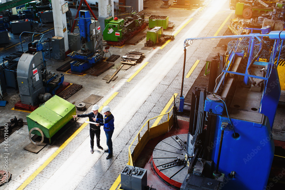 Fototapeta premium The chief engineer in a white protective helmet and his assistant conduct an inspection of the plant's production premises