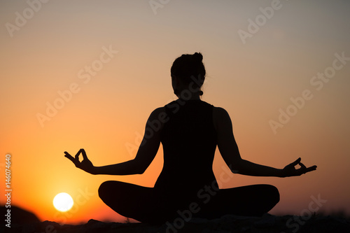 Slim woman doing yoga over orange sun