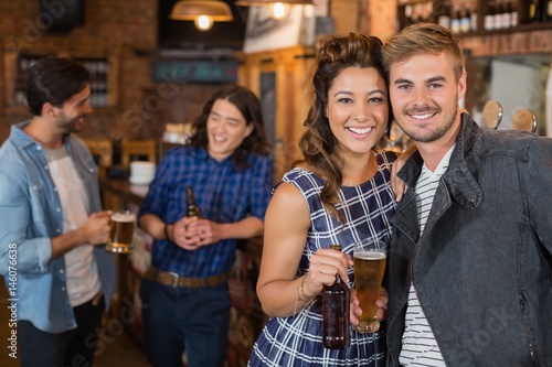 Smiling friends holding beer glass and bottle in pub