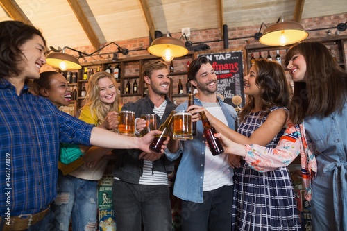 Happy friends toasting beer glasses and bottles in pub