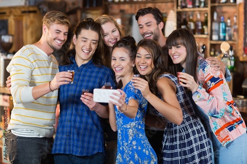 Cheerful friends taking selfie while holding short glasses