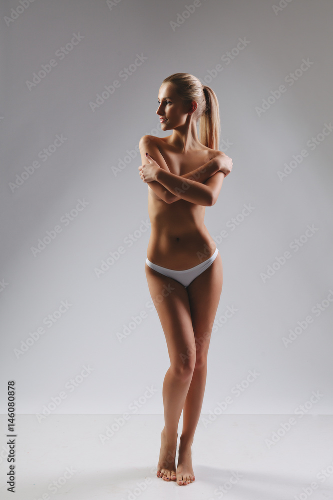 Slim tanned woman with perfect skin. Isolated over gray background - obrazy, fototapety, plakaty 