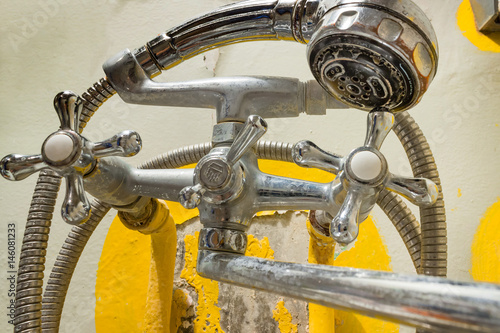 Old rusty shower tap on the background of a painted concrete wall with cracked paint. Poverty