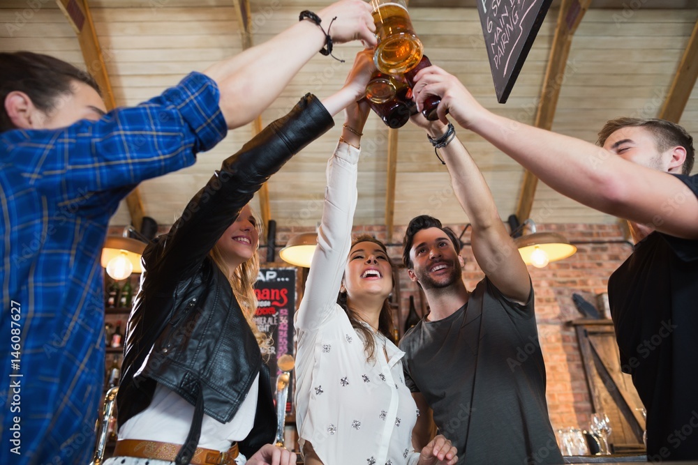 Fototapeta premium Cheerful friends toasting beer bottles and mugs
