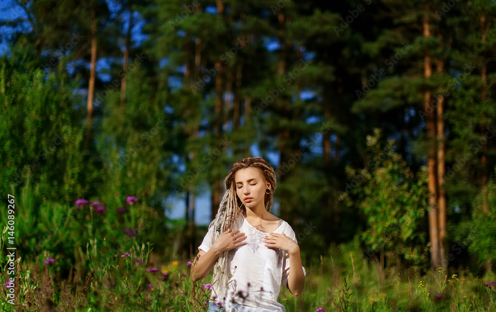 Young girl with long dreadlocks in blue jeans, walking through the field among flowers and trees, Summer vacation in the forest concept Young girl with long dreadlocks in blue jeans, walking through the field among flowers and trees, Summer vacation in the forest concept