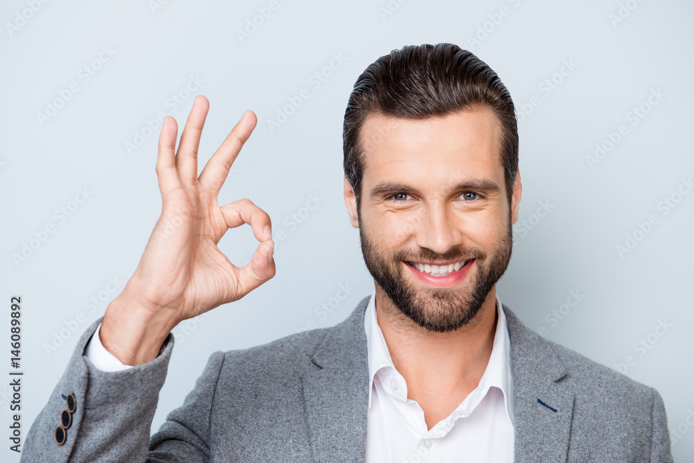 Close up photo of happy man with stylish hairdo and in formalwear showing ok-sign on gray background Close up photo of happy man with stylish hairdo and in formalwear showing ok-sign on gray background