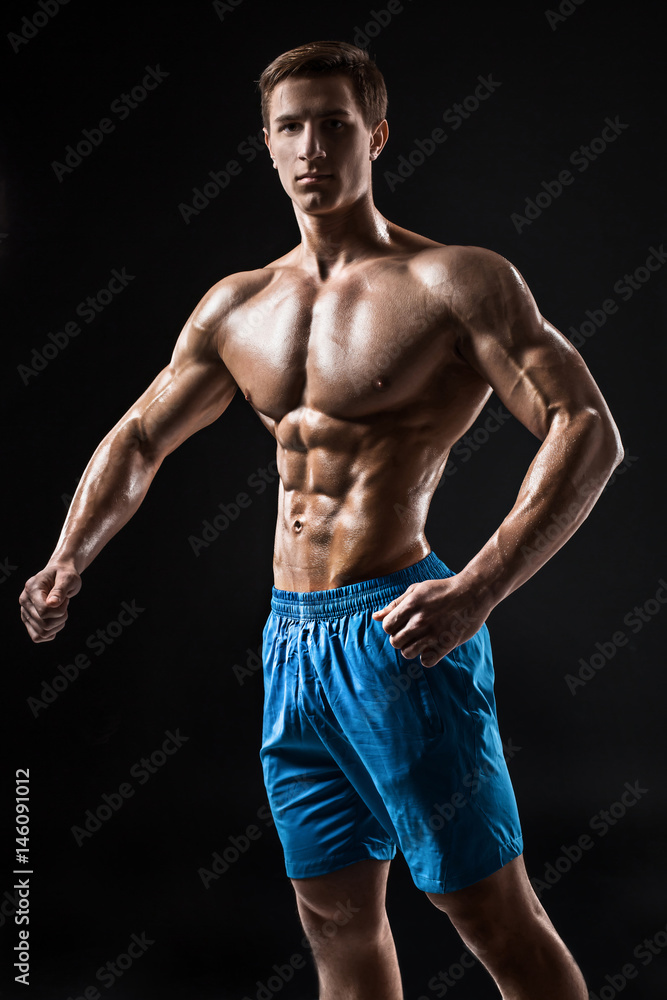 Muscular and fit young bodybuilder fitness male model posing over black background. Muscular and fit young bodybuilder fitness male model posing over black background.