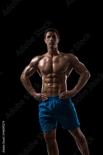 Muscular and fit young bodybuilder fitness male model posing over black background.