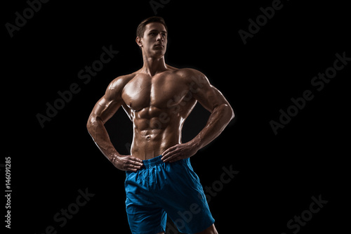 Muscular and fit young bodybuilder fitness male model posing over black background. © nazarovsergey