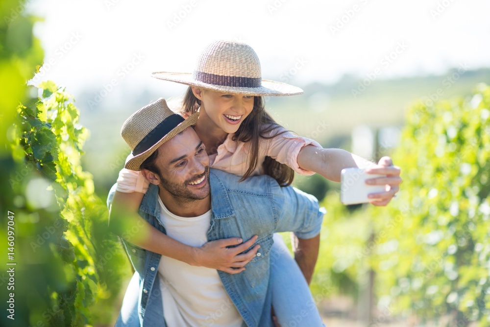 Obraz premium Happy couple taking selfie while piggybacking at vineyard