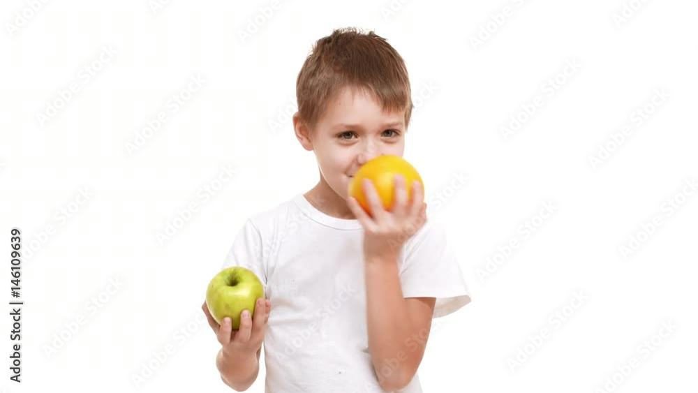 Young smiling Caucasian boy holding big apple and orange in hands exploring them smelling and choosing orange. White background Young smiling Caucasian boy holding big apple and orange in hands exploring them smelling and choosing orange. White background