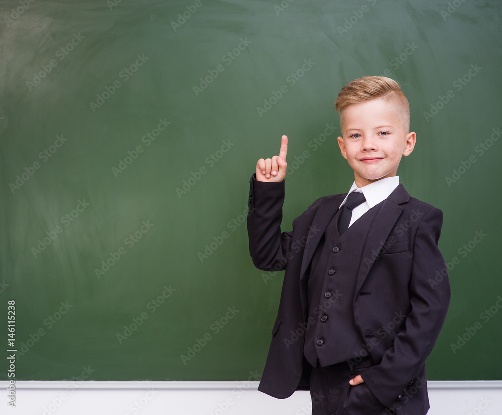 Happy boy in a suit points on empty green chalkboard Happy boy in a suit points on empty green chalkboard