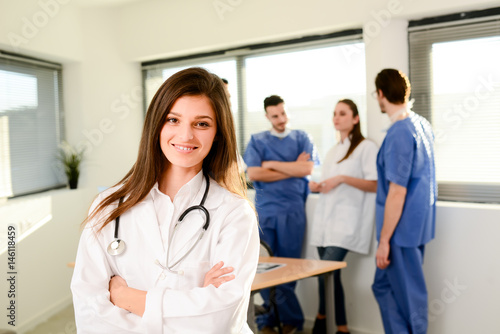 portrait of a young female doctor residential student in hospital office with medical team in background