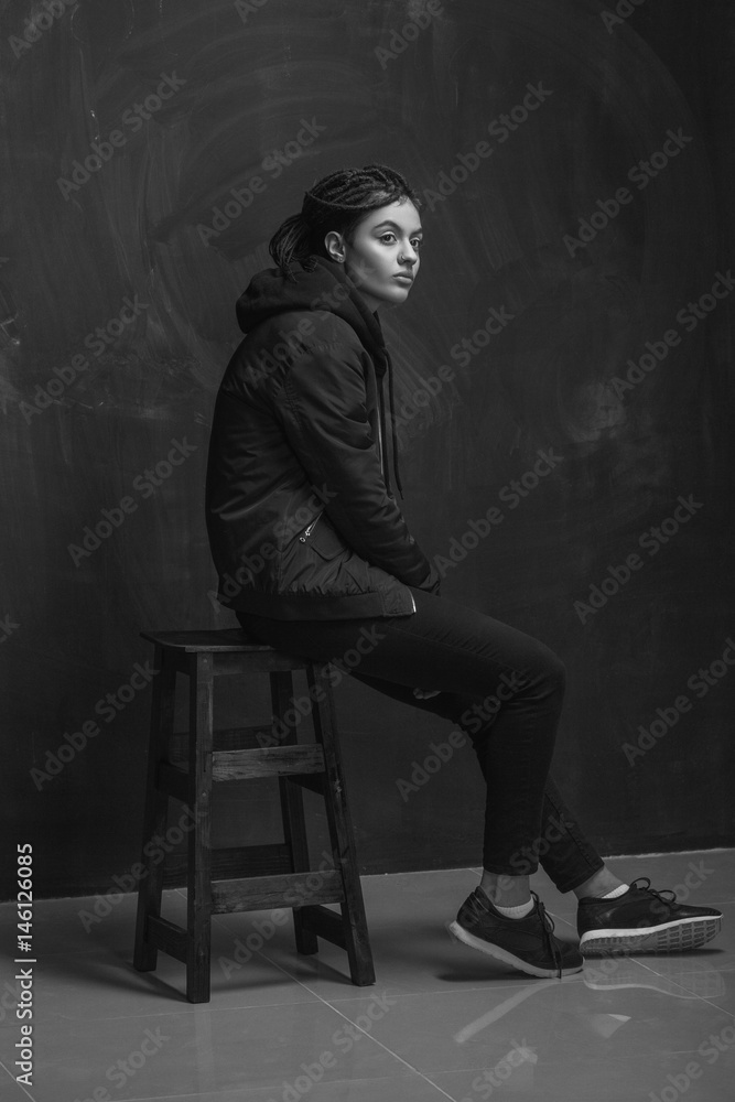 Beautiful fashion model sitting on stool against wall Beautiful fashion model sitting on stool against wall