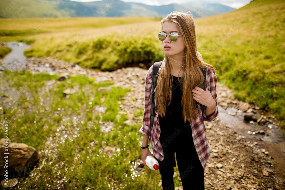 Young woman hiker hiking in beautiful mountains. Woman hiker enjoying amazing landscapes near mountain stream.