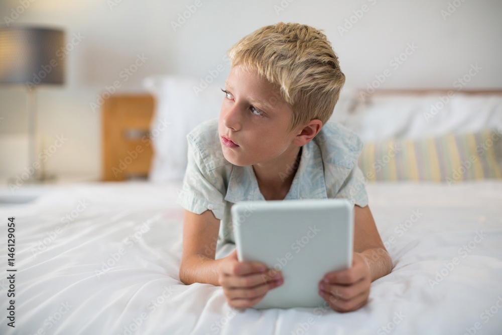 Thoughtful boy with digital tablet lying on bed Thoughtful boy with digital tablet lying on bed