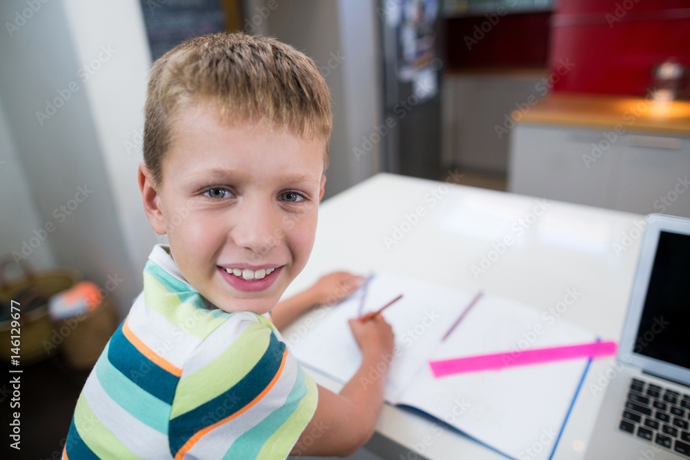 Smiling boy doing his homework in kitchen Smiling boy doing his homework in kitchen