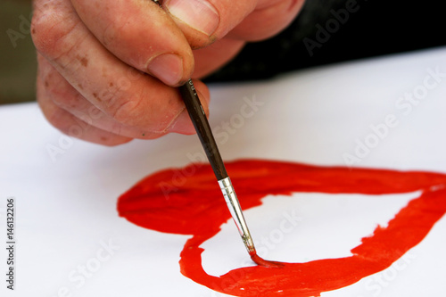 Man s hand draws a red heart with watercolor