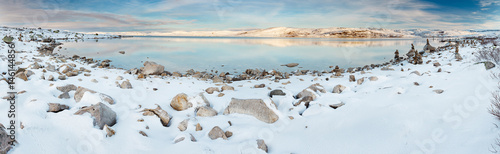 Panoramic view of norwegian lake at sunset. There are stone columns on rocks covered with snow.