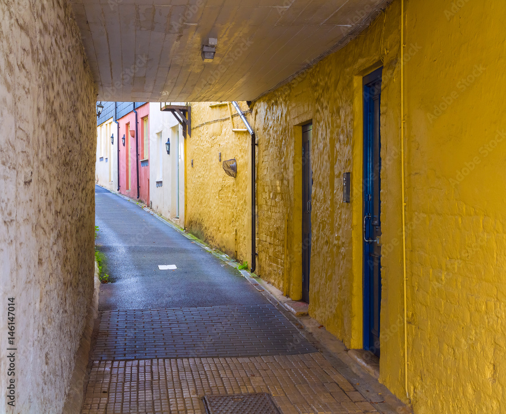 A small street with a tunnel. Bright yellow and red and white walls. Blue doors. Honiton. Devon