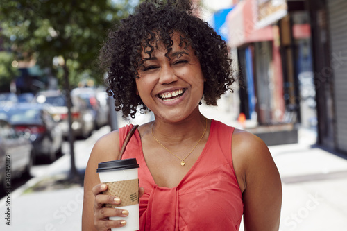 Smiling woman carrying coffee on city sidewalk