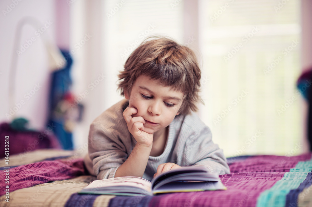 Cute little boy lying on bed reading book Cute little boy lying on bed reading book