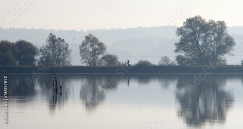 A cyclist at dawn rides along the shore of the lake. Reflection in the water.