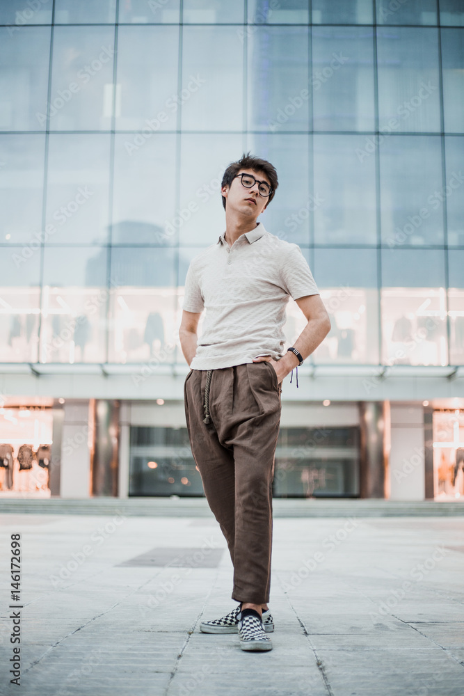 Young asian boy posing on the street without technology devices. Wearing a polo and wide pants. Man with hands in pockets
