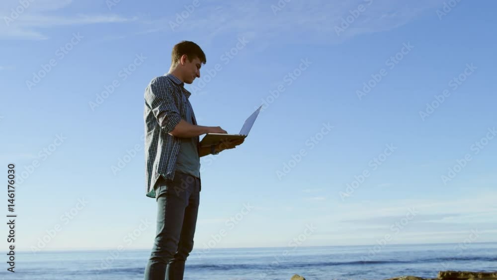 Young beautiful man is chatting with someone on a coast by using his laptop Young beautiful man is chatting with someone on a coast by using his laptop