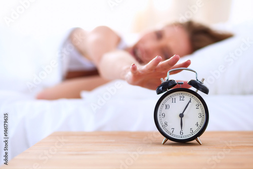 Young sleeping woman and alarm clock in bedroom at home