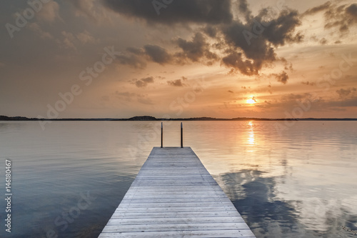 Beautiful glowing orange sunset over a rustic timber plank jetty reflected in the mirror calm waters of the sea below, a background of natural beauty and serenity. Northern sea, Sweden, Scandinavia.