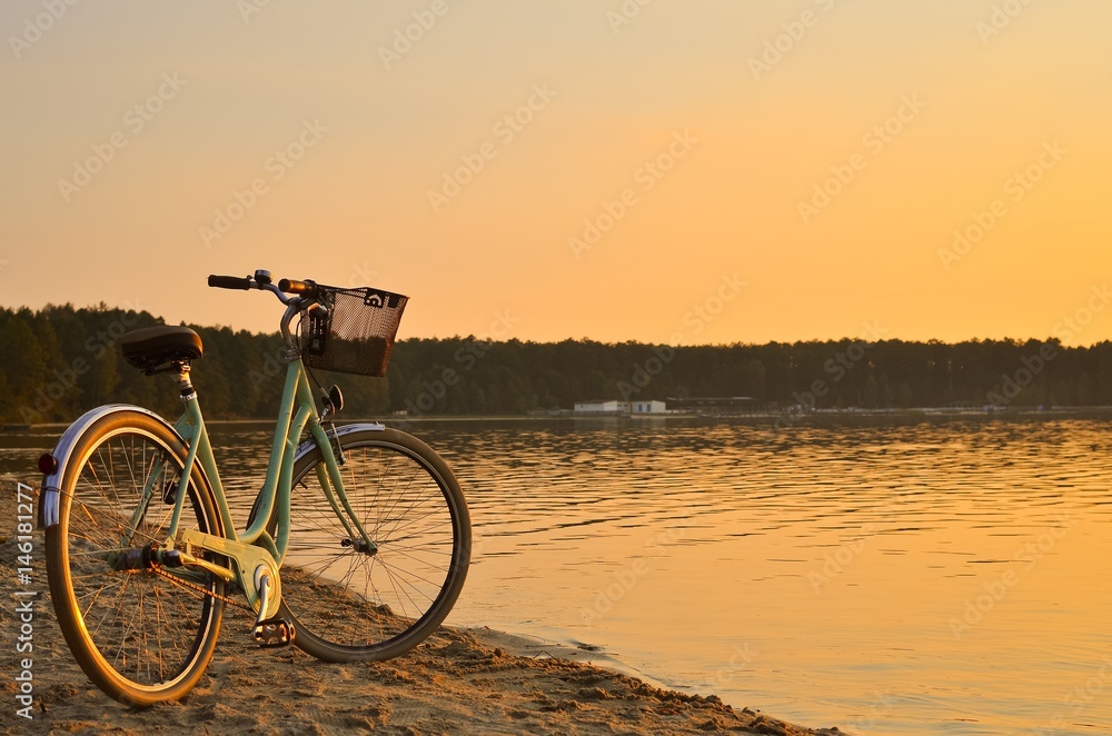 Vintage bicycle with a basket near the lake during beautiful summer sunset. Copy space.
