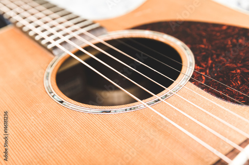 Close up of steel strings on an acoustic guitar. Cedar top with textured pickguard and ornate design around sound hole.