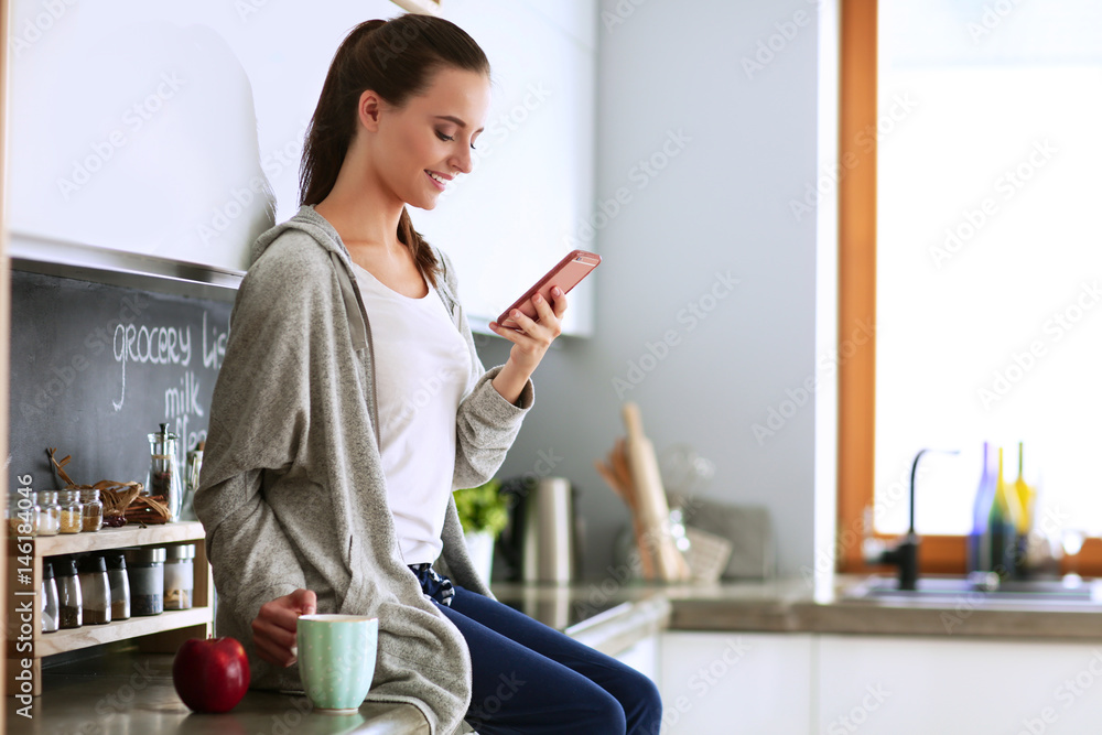 Woman using mobile phone sitting in modern kitchen