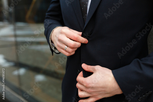 Closeup of a businessman buttoning a button in a black suit against the background of the business center with copy space